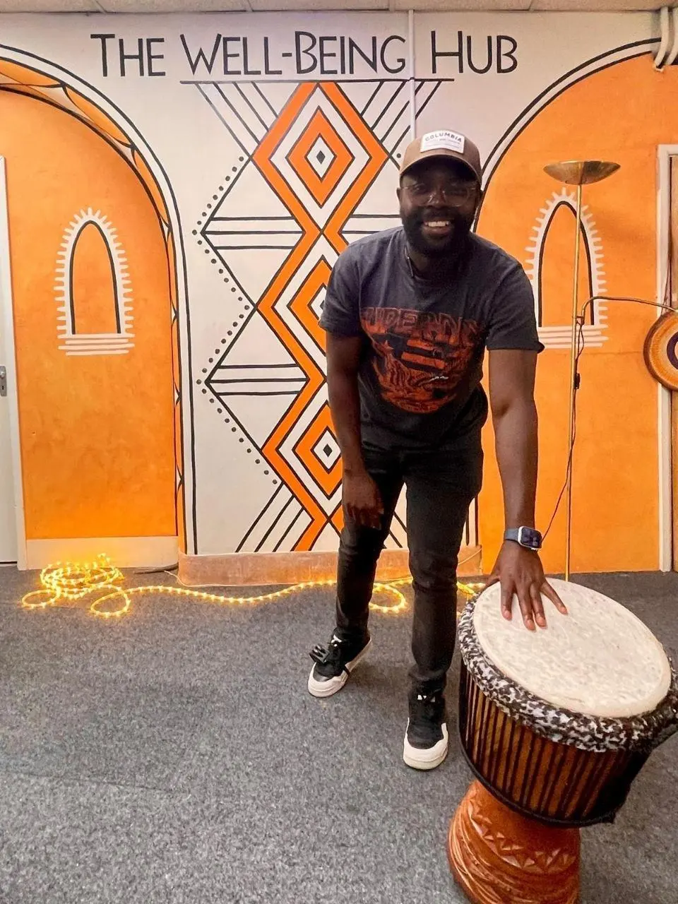 A musician playing djembe in front of the Wellbeing Hub mural