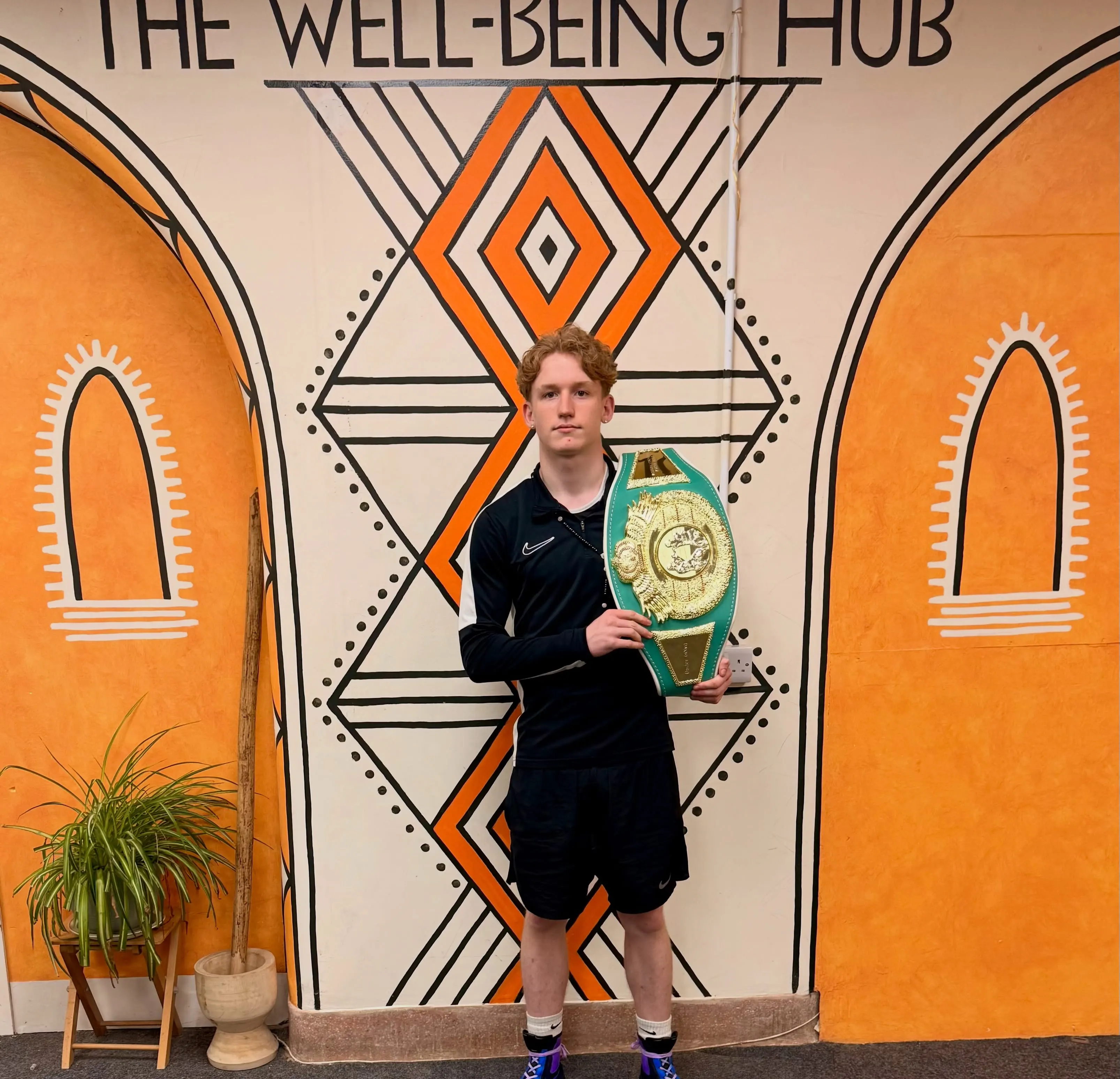 A young member of the Hub community proudly holding a boxing championship belt in front of the Hub mural