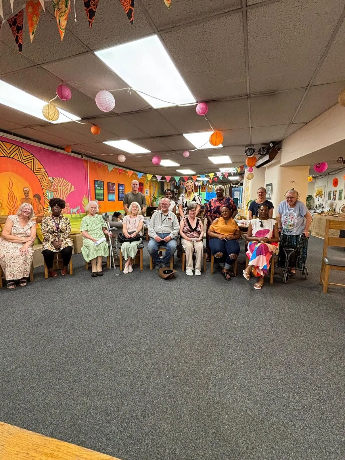 A group from The Wellbeing Hub together in the community space, in front of the African mural