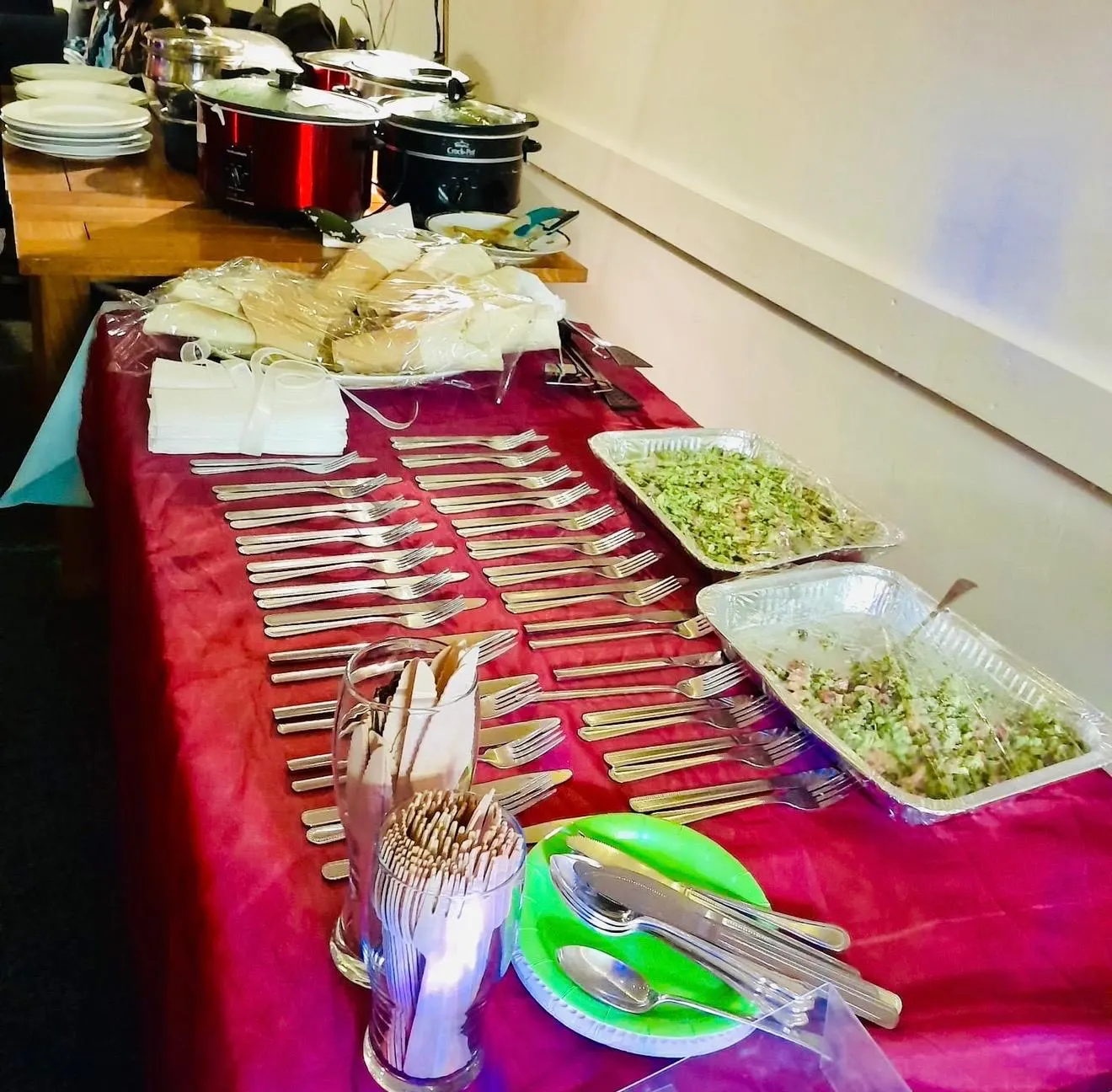 A long table laid for a Hub community food evening, with slow cookers, trays of greens and cutlery set out for everyone