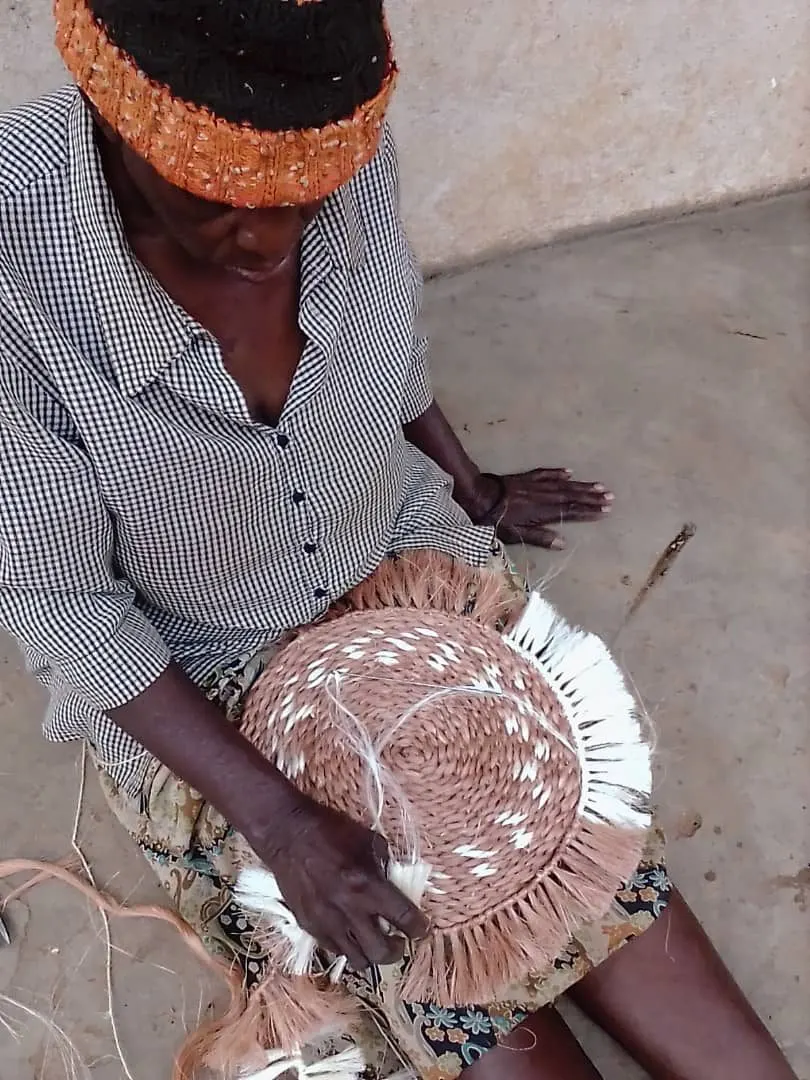 A woman seated on the ground weaving a large round basket by hand