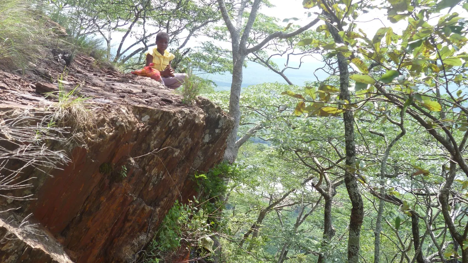 A person sitting quietly on a rock ledge looking out over a wooded valley
